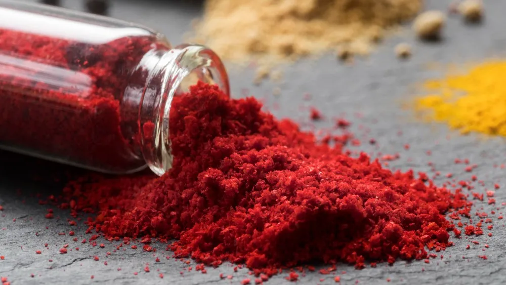 Red root powder in glass jar spilled on table, traditional herbal remedy for circulation.